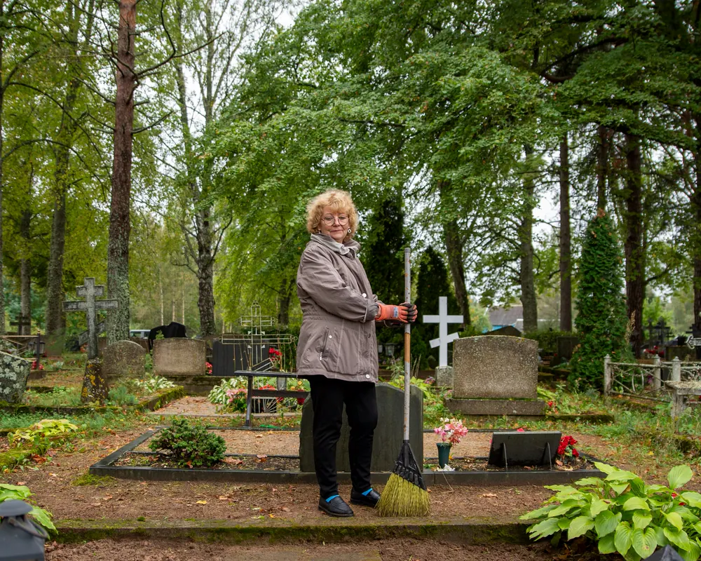 Une femme entretient une sépulture dans un cimetière arboré
